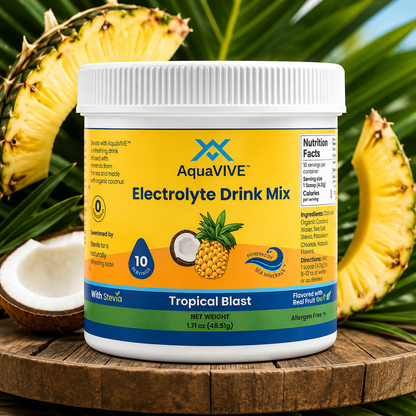 A tub of AquaVIVE Electrolyte Drink Mix in Tropical Blast flavor, styled on a wooden surface with sliced pineapples and a coconut half in the background.